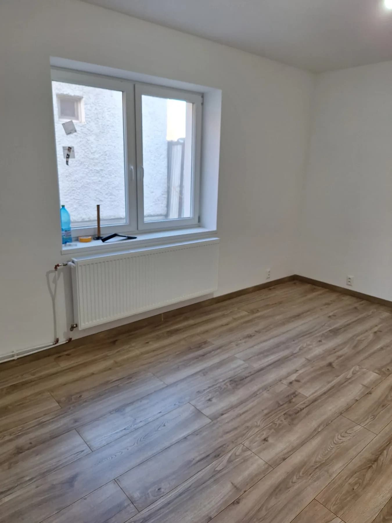 Dokončená izba s bielymi stenami, novým radiátorom a podlahou
